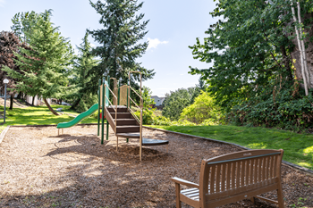 A playground with a green slide and a wooden bench.